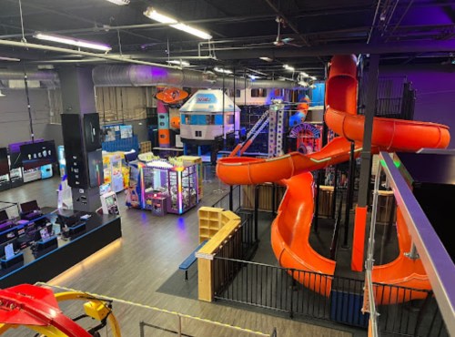 A colorful indoor play area featuring slides, climbing structures, and arcade games in a spacious setting.