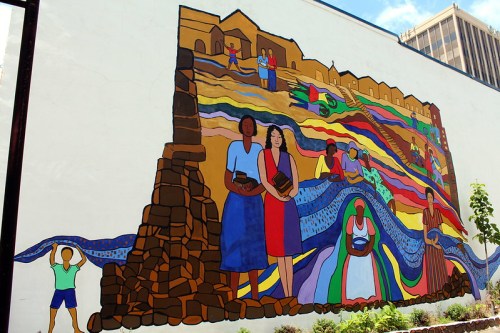 Colorful mural depicting people carrying goods and vibrant patterns, showcasing community and cultural heritage.