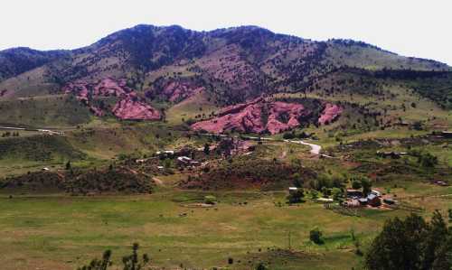 A scenic view of rolling green hills and rocky mountains under a clear sky, with a small settlement in the valley.