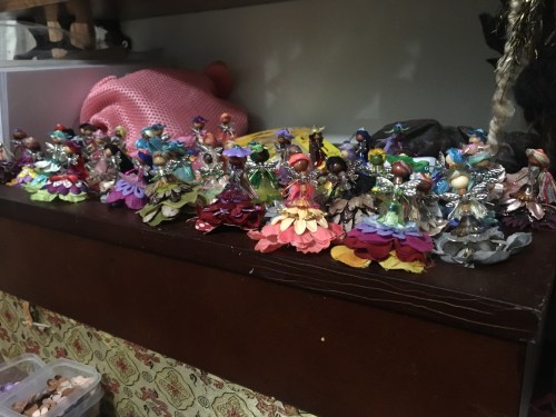 A colorful display of small fairy figurines arranged on a shelf, surrounded by various decorative items.