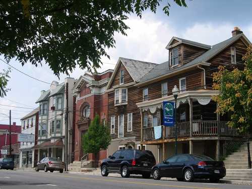 A street view featuring a mix of historic buildings, including a wooden inn and a brick structure, with parked cars.