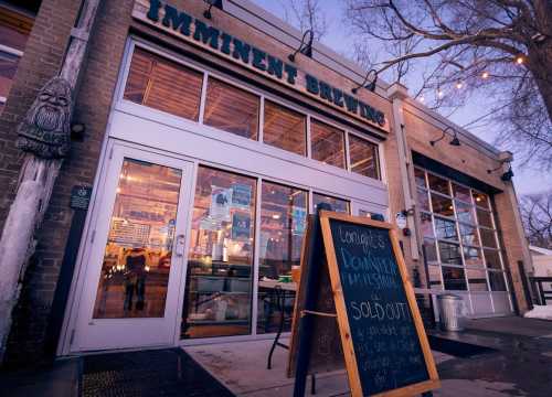 Exterior of Imminent Brewing with a chalkboard sign announcing a sold-out film festival. Warm evening lighting.