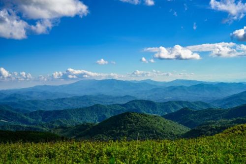 A panoramic view of rolling green hills under a bright blue sky with fluffy white clouds.