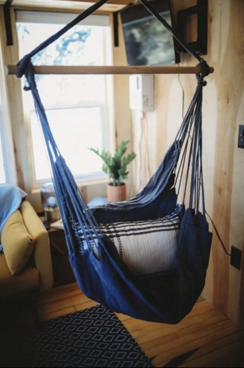 A cozy indoor hammock hangs from a wooden beam, with a plant and a TV visible in the background.