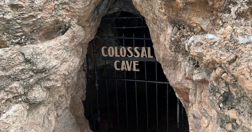 Entrance to Colossal Cave, featuring a wooden sign and rocky surroundings.