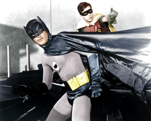 Batman and Robin in colorful costumes, striking a heroic pose next to the Batmobile.