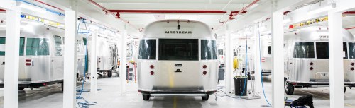 A row of shiny Airstream trailers in a well-lit manufacturing facility.