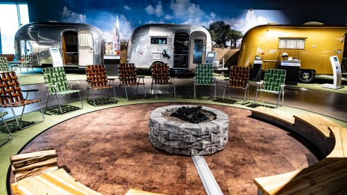 A cozy gathering space with chairs around a stone fire pit, featuring vintage Airstream trailers in the background.
