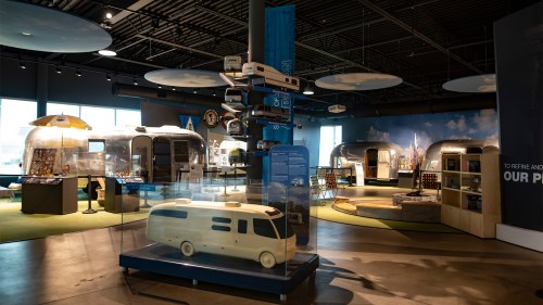A modern exhibit featuring vintage trailers and a wooden model, with informative displays and a bright, open space.