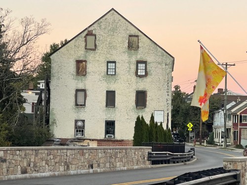 A weathered, boarded-up building with a colorful flag nearby, set against a pastel sunset sky.