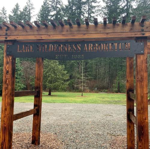 Wooden entrance sign for Lake Wilderness Arboretum, established 1963, surrounded by trees and gravel path.