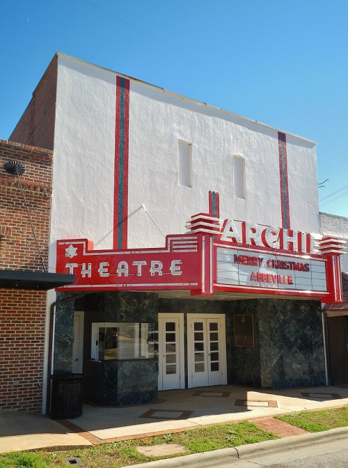 Historic Archie Theatre with a festive "Merry Christmas" sign, featuring a vibrant red and green marquee against a blue sky.