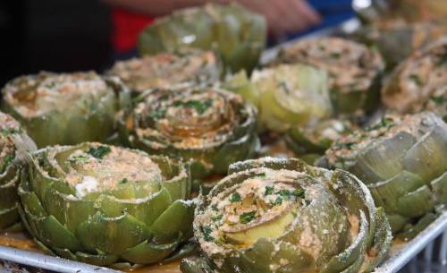 A tray of stuffed artichokes, filled with a mixture and garnished with herbs, ready to be served.