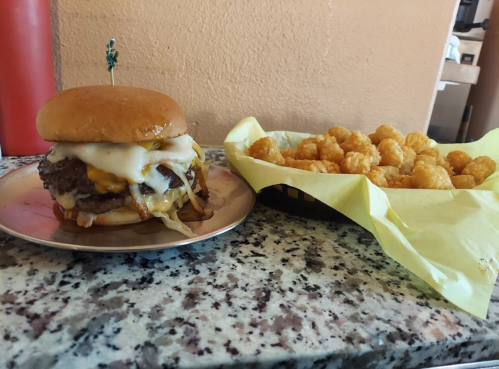 A juicy cheeseburger with melted cheese and toppings on a plate, alongside a basket of golden tater tots.