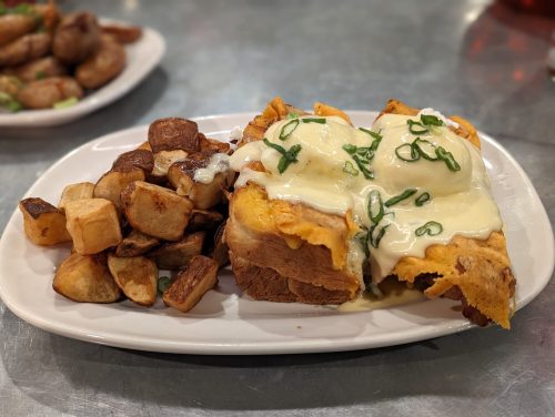 A plate of cheesy enchiladas topped with green onions, served with crispy potato cubes on the side.