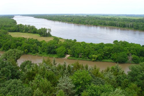 A scenic view of a wide river winding through lush green trees and fields under a clear sky.