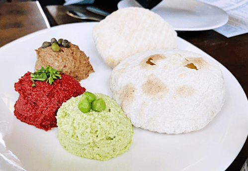 A plate with three colorful dips—red, green, and brown—accompanied by two round, white flatbreads.