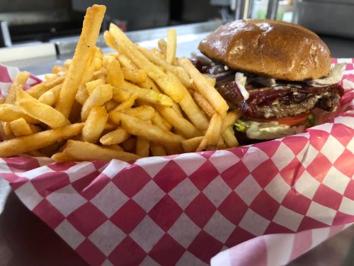 A delicious burger with lettuce, tomato, and grilled meat, served with a side of golden French fries in a checkered basket.