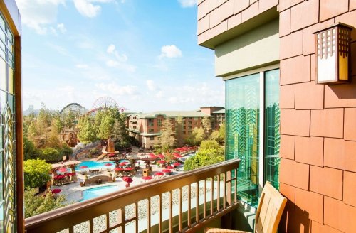 View from a balcony overlooking a resort pool area with red umbrellas and amusement park rides in the background.