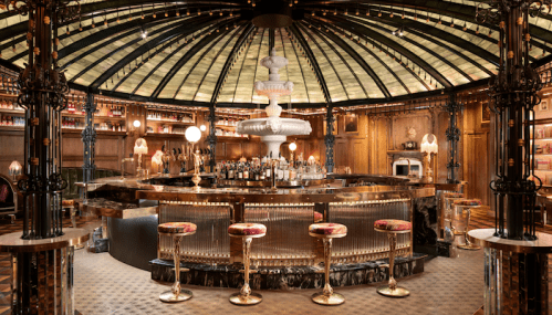 A luxurious bar with a domed glass ceiling, ornate decor, and elegant seating around a polished counter.