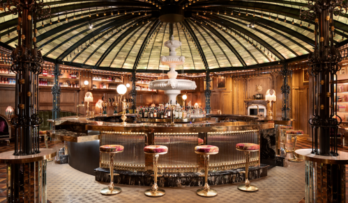 A luxurious bar with a domed glass ceiling, ornate decor, and elegant seating around a central fountain.