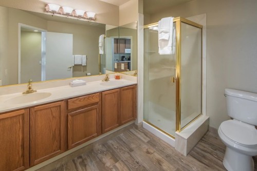 A modern bathroom featuring a shower, wooden vanity, and a toilet, with neutral walls and warm lighting.