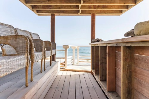 View from a beachside pavilion with wooden flooring, wicker chairs, and a table overlooking the ocean.