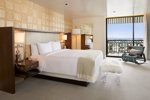 A modern hotel room featuring a king bed, stylish decor, a balcony with a view, and a cozy seating area.