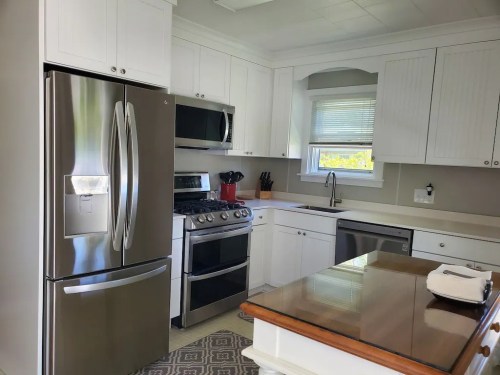Modern kitchen featuring stainless steel appliances, white cabinets, and a wooden countertop. Bright and spacious design.