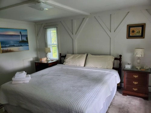 Cozy bedroom with a large bed, white linens, a nightstand, and a painting of a lighthouse on the wall.