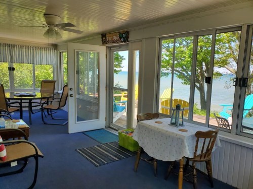 Bright sunroom with a table, chairs, and large windows overlooking a lake and colorful outdoor seating.