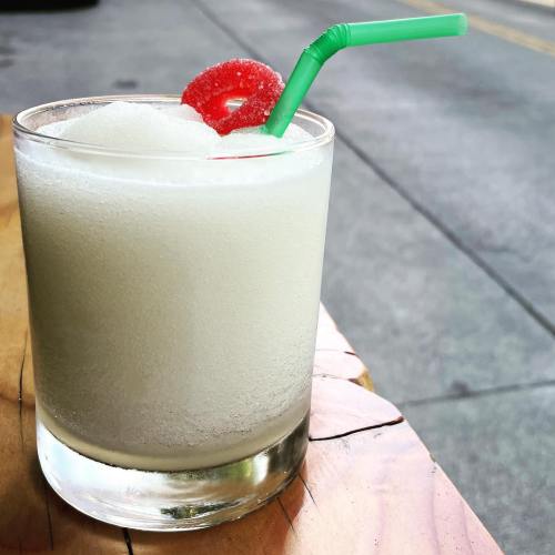 A frosty drink in a glass with a green straw and a cherry on top, sitting on a wooden table.