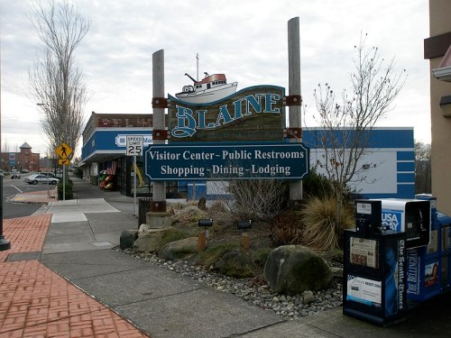 Sign for Blaine, featuring visitor center, restrooms, shopping, dining, and lodging, with a boat in the background.