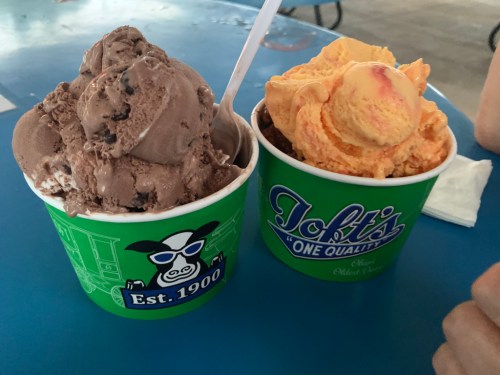 Two ice cream cups on a blue table: one with chocolate and cookies, the other with orange sherbet.