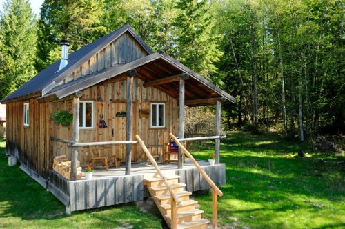 A rustic wooden cabin surrounded by trees, featuring a porch and steps leading up to the entrance.