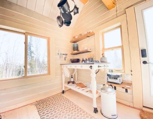 Cozy kitchen corner with a wooden table, shelves, and large windows letting in natural light.