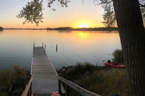 A serene sunset over a calm lake, with a wooden dock leading to the water and a kayak nearby.