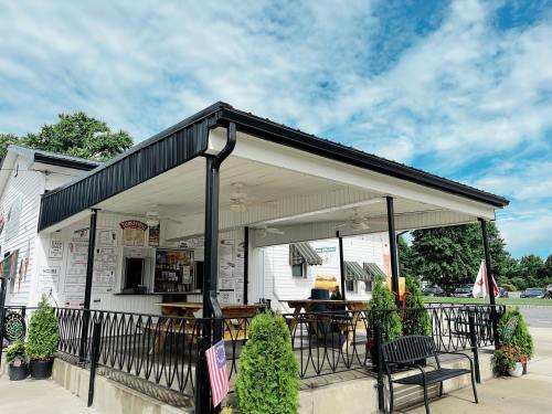 A small outdoor eatery with a covered patio, featuring tables and a menu board, set against a blue sky.