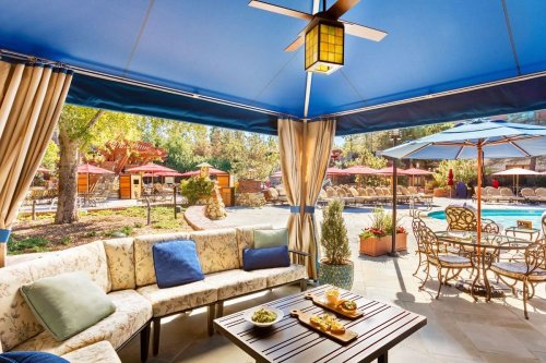 Cozy outdoor seating area with a table, snacks, and a view of a pool surrounded by umbrellas and lounge chairs.