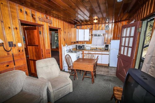 Cozy cabin interior with wooden walls, a small kitchen, dining table, and seating area.