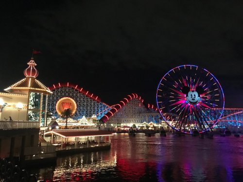 Colorful amusement park at night featuring a large Ferris wheel and illuminated roller coaster over water.