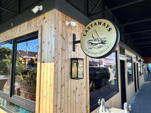 Sign for "Castaways Seafood Grille" on a wooden exterior, with an "open" sign visible in the window.