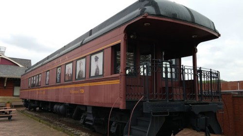 A vintage train car with historical photographs displayed on its side, set against a cloudy sky.