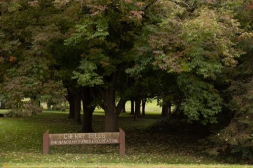 Sign for Cherry Hills, surrounded by lush green trees in a park setting.