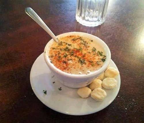 A small bowl of creamy soup topped with herbs and spices, served with a few crackers on a white plate.