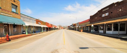 A quiet, empty street lined with historic brick buildings and shops under a clear blue sky.