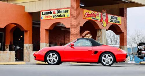 A red convertible sports car parked outside a restaurant with a sign for lunch and dinner specials.