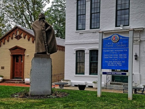 Statue of a historical figure in front of a building, with a sign detailing the history of Perth Amboy, NJ.