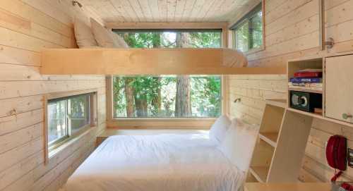 Cozy wooden cabin interior with a bunk bed and a double bed, surrounded by large windows and natural light.