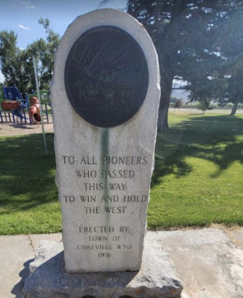 A stone monument honoring pioneers, with an inscription about their journey to win and hold the West, in a park setting.